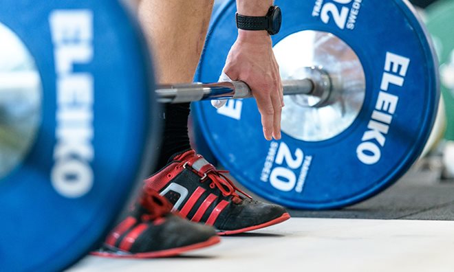 A person standing over a barbell with blue weights on it