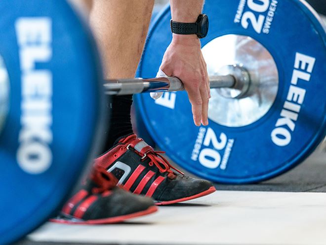 A person standing over a barbell with blue weights on it