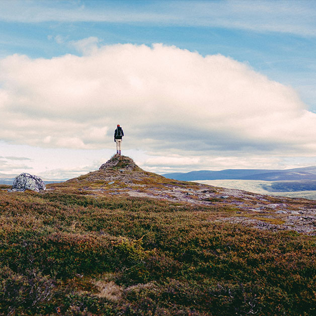 A person standing alone on top of a small hill overlooking a mountain range