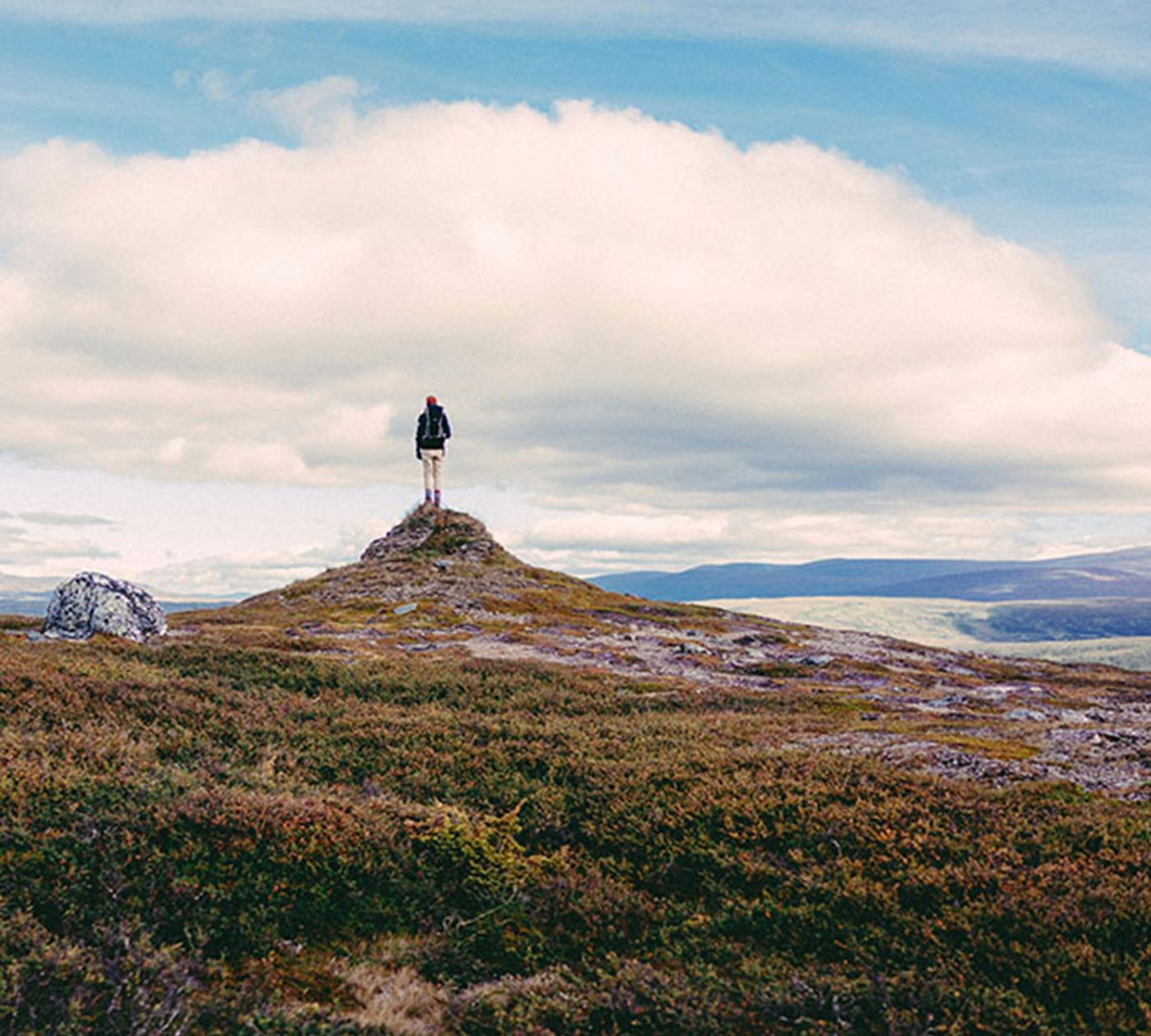A person standing alone on top of a small hill overlooking a mountain range